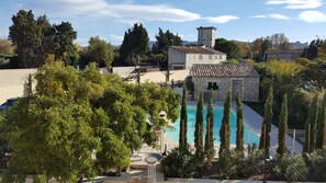 Un edificio de piedra con piscina, rodeado de árboles altos y un cielo despejado.