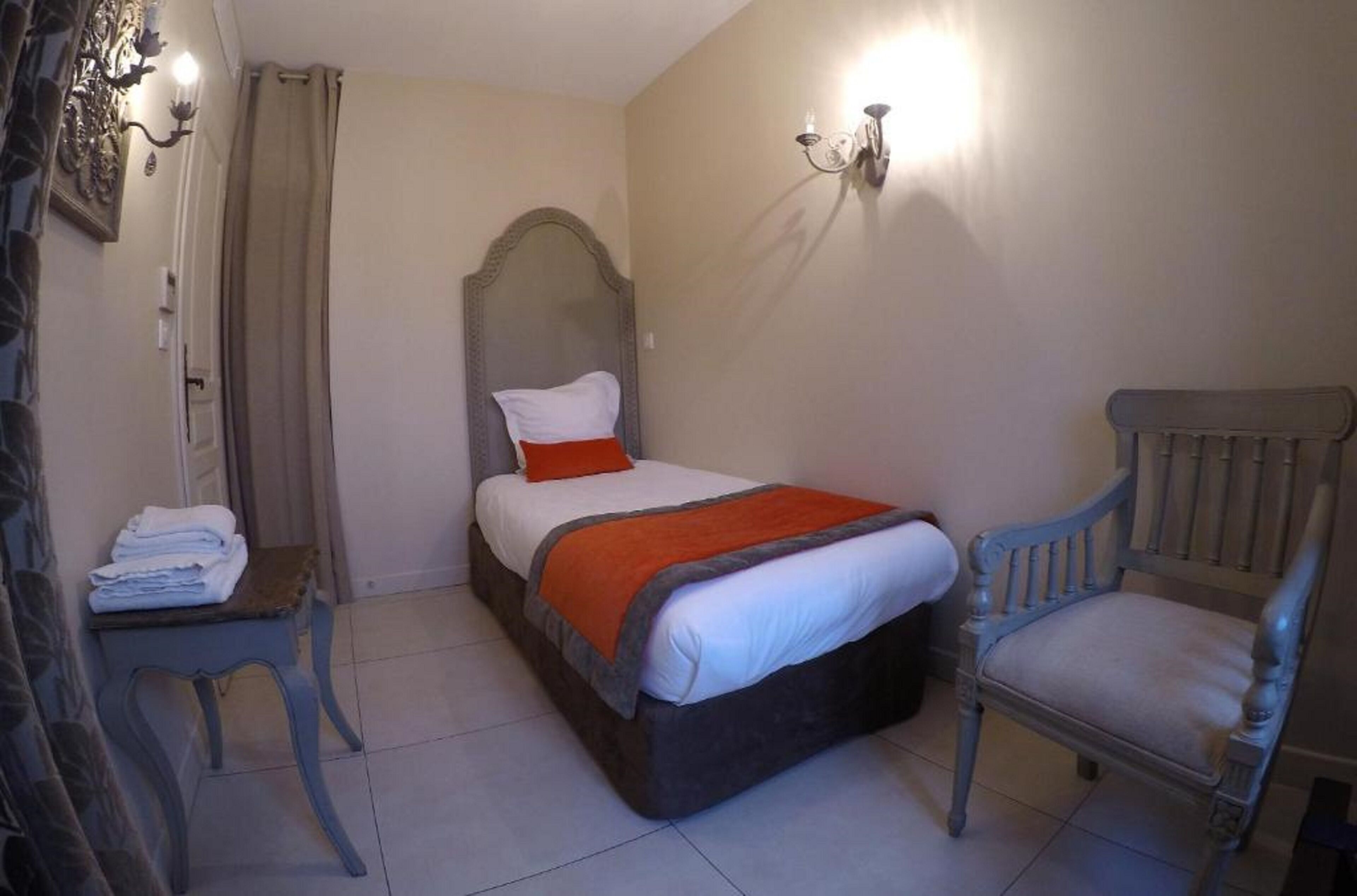 A bedroom with a bed, a chair, a table, and a wall-mounted light fixture.
