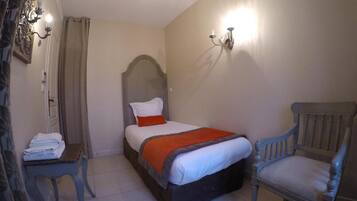 A bedroom with a bed, a chair, a table, and a wall-mounted light fixture.