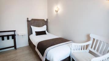 Quarto com cama de madeira, roupa de cama branca, cadeira branca e luminária fixada na parede.