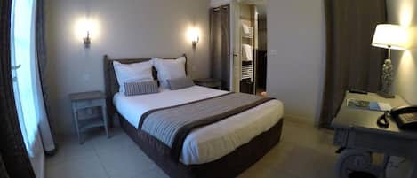 Una habitación de hotel con cama, mesita de noche, lámpara y escritorio con teléfono.