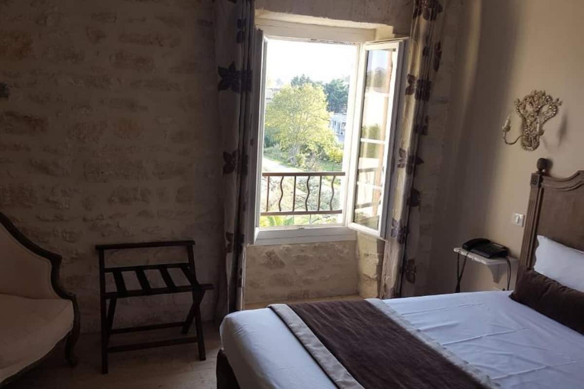Une chambre à coucher comprenant un lit, une chaise, une petite table et une fenêtre donnant sur un balcon.