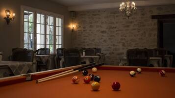A billiards room with a pool table, chairs, and a chandelier.