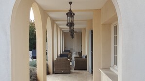 A covered outdoor area with a tiled floor, arched columns, and a hanging light fixture. - Hôtel Le Mas Saint-Joseph (St.-Rémy-de-Provence)
