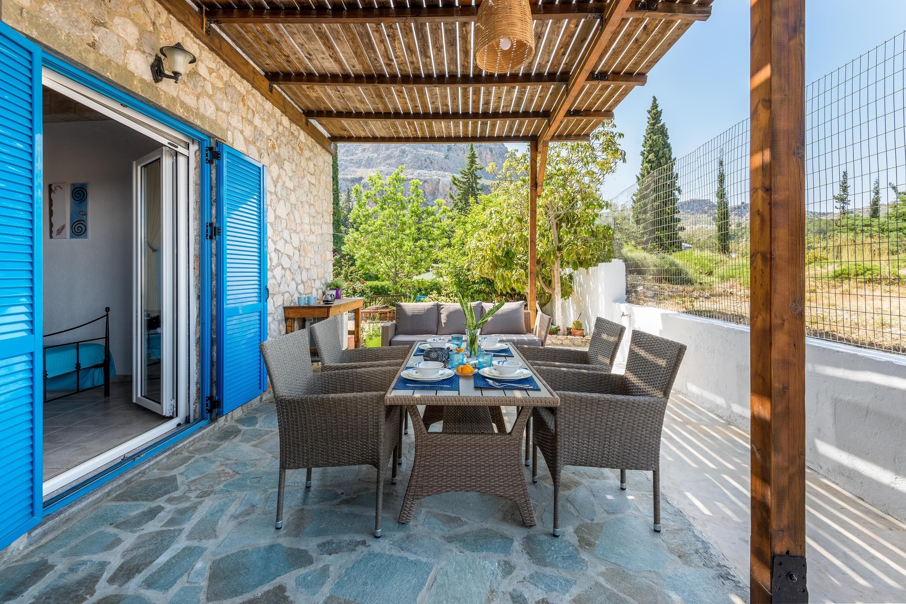 A covered outdoor seating area with wicker furniture, a stone floor, and a view of greenery and mountains.