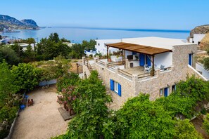 A coastal property with a stone building, a patio with outdoor furniture, and a view of the sea. - Agnanti Beach Studios (Rhodes)