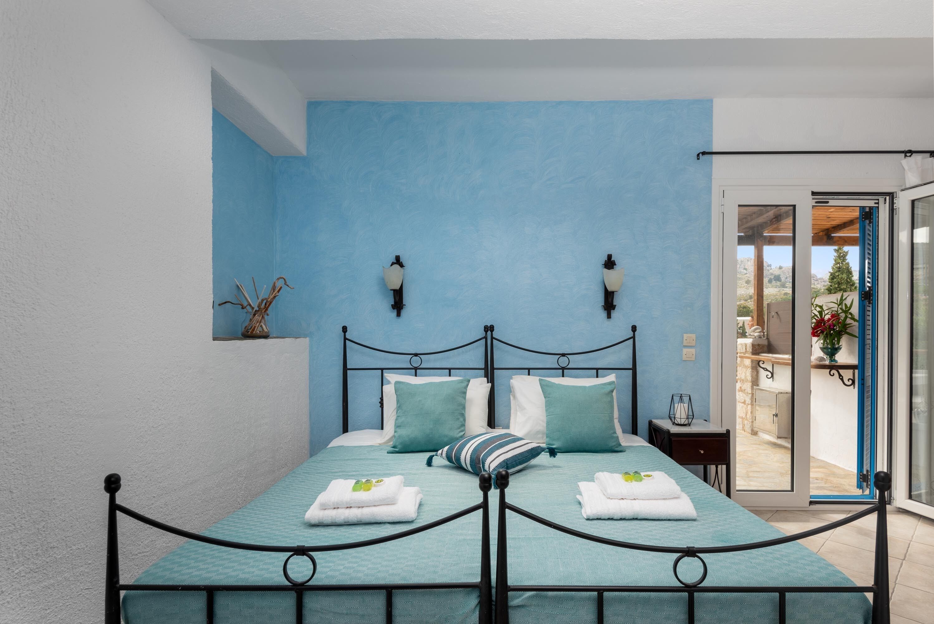 A bedroom with a bed, two wall-mounted lights, a window, and a view of the outdoors.