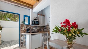 Una cocina compacta con microondas, lavamanos y armarios, una mesa de comedor con sillas, y un florero con flores.