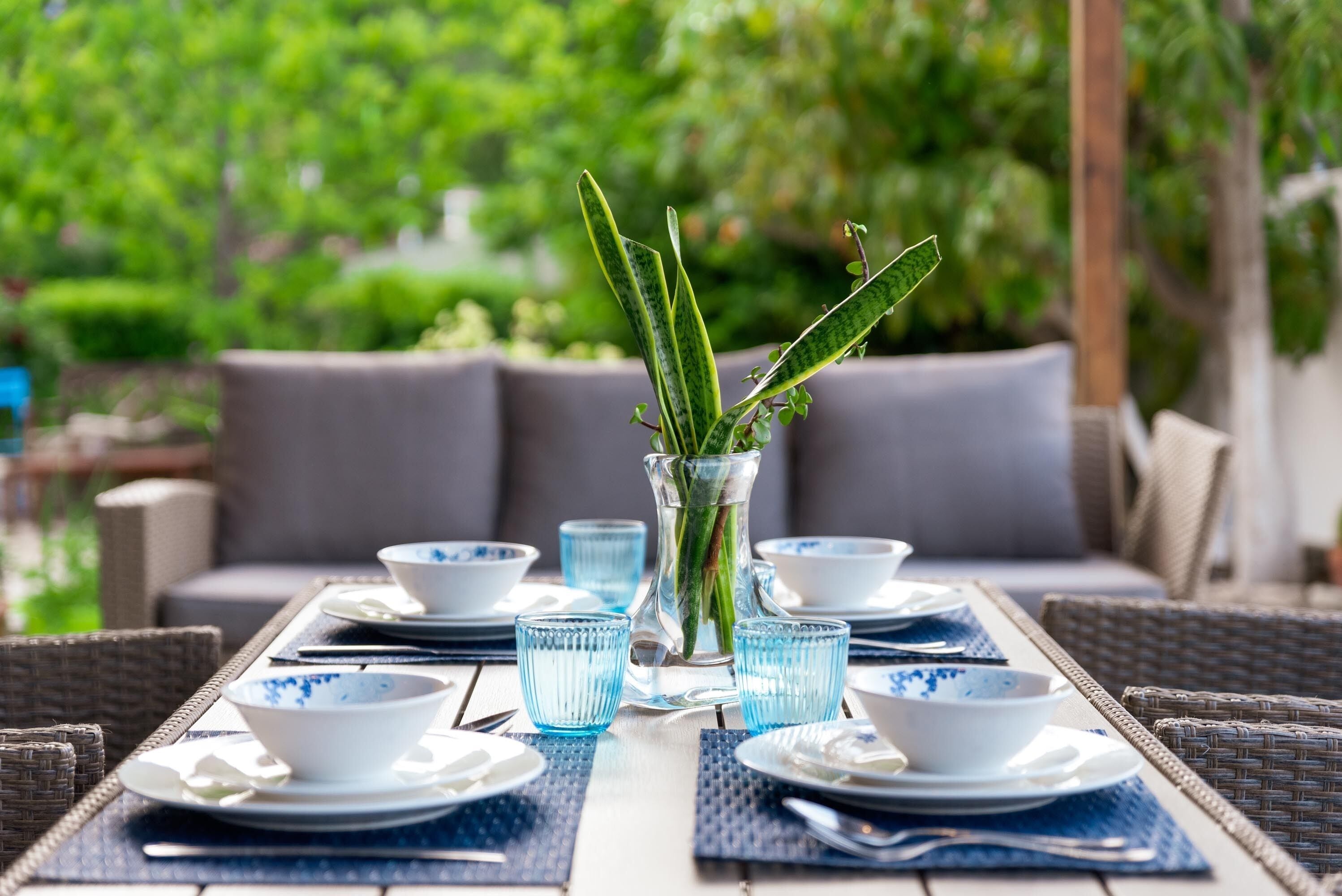 A table set with white and blue patterned bowls, clear glass cups, and a vase with green plants.