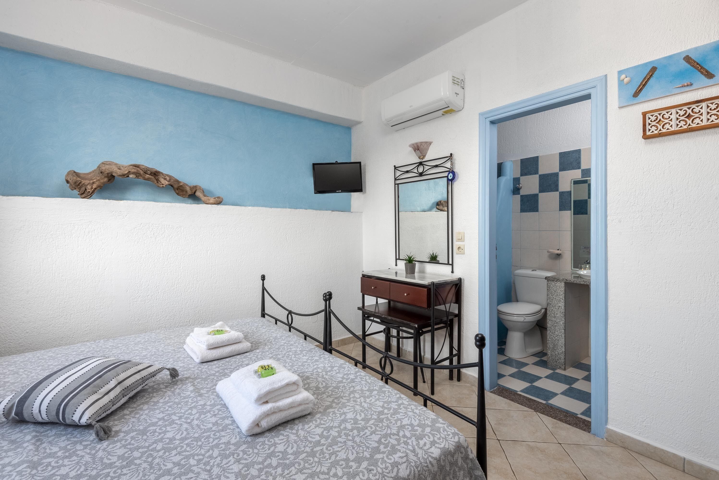 A bedroom with a bed, a desk, a mirror, and a bathroom with a checkered floor.