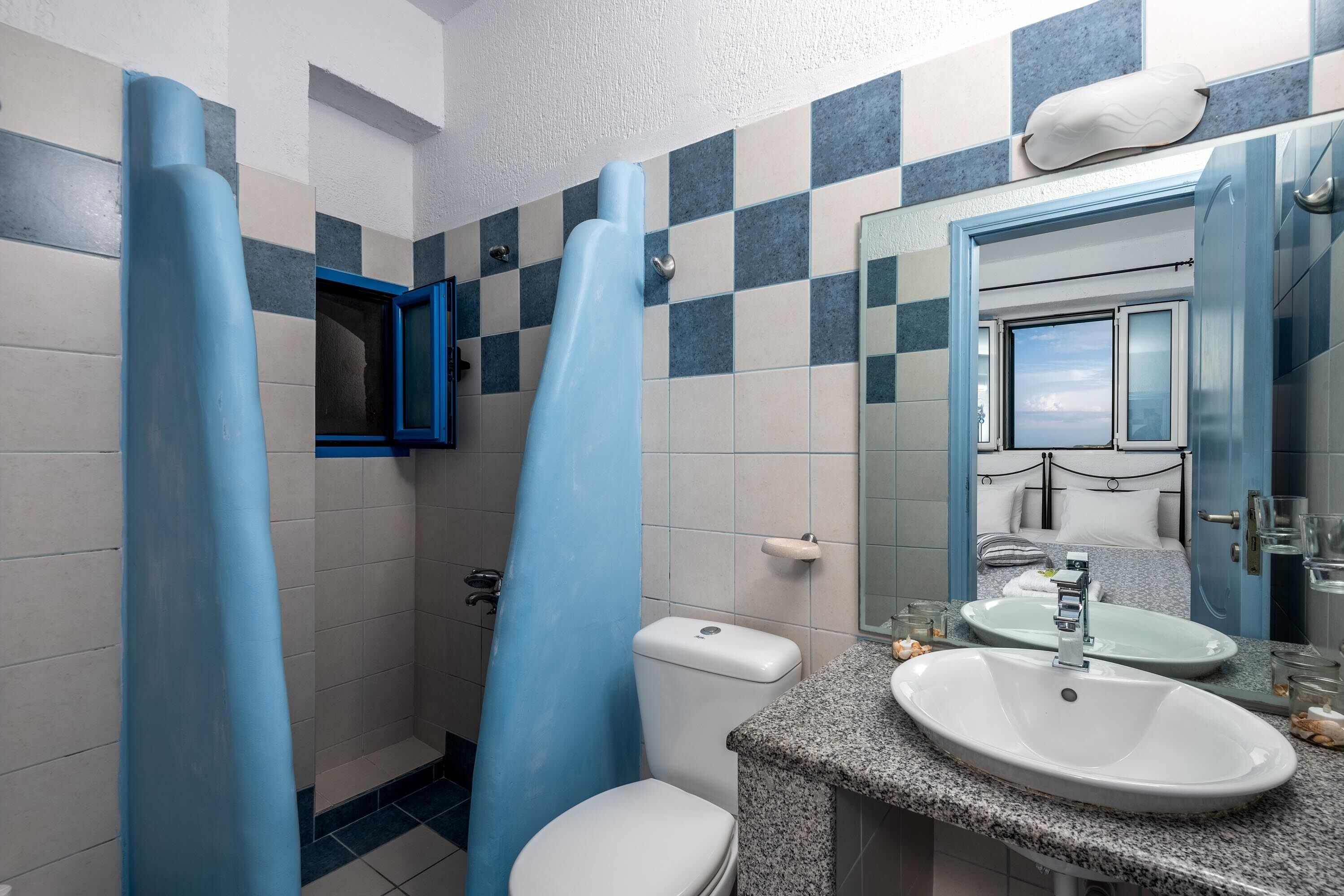 A bathroom with a toilet, sink, and mirror. There are blue shower curtains and a window with a view.