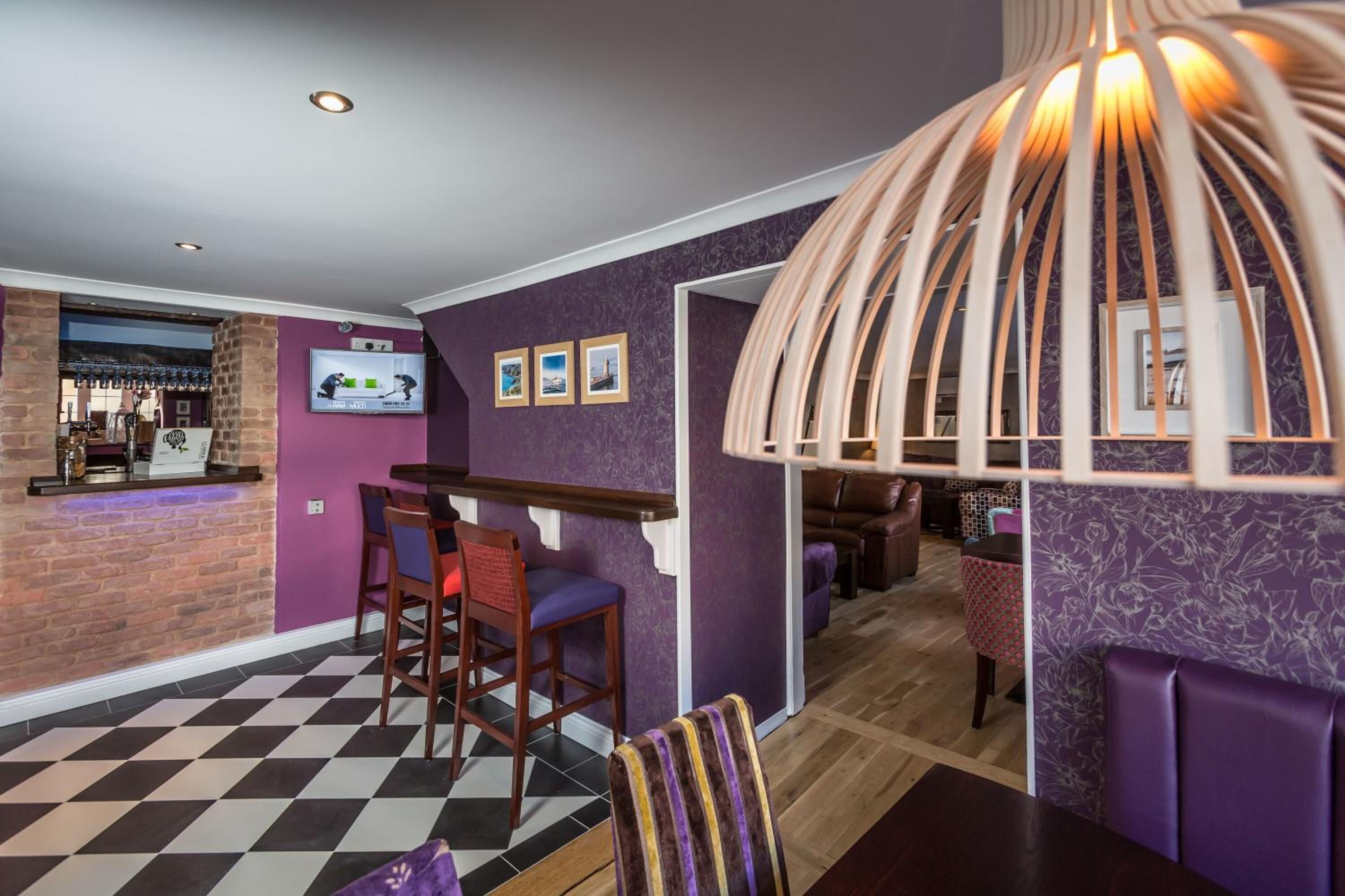 A modern bar area with a checkered floor, purple walls, and a unique wooden light fixture.