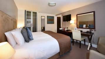 Una habitación de hotel con una cama grande, un escritorio, una silla, un televisor y un espejo.