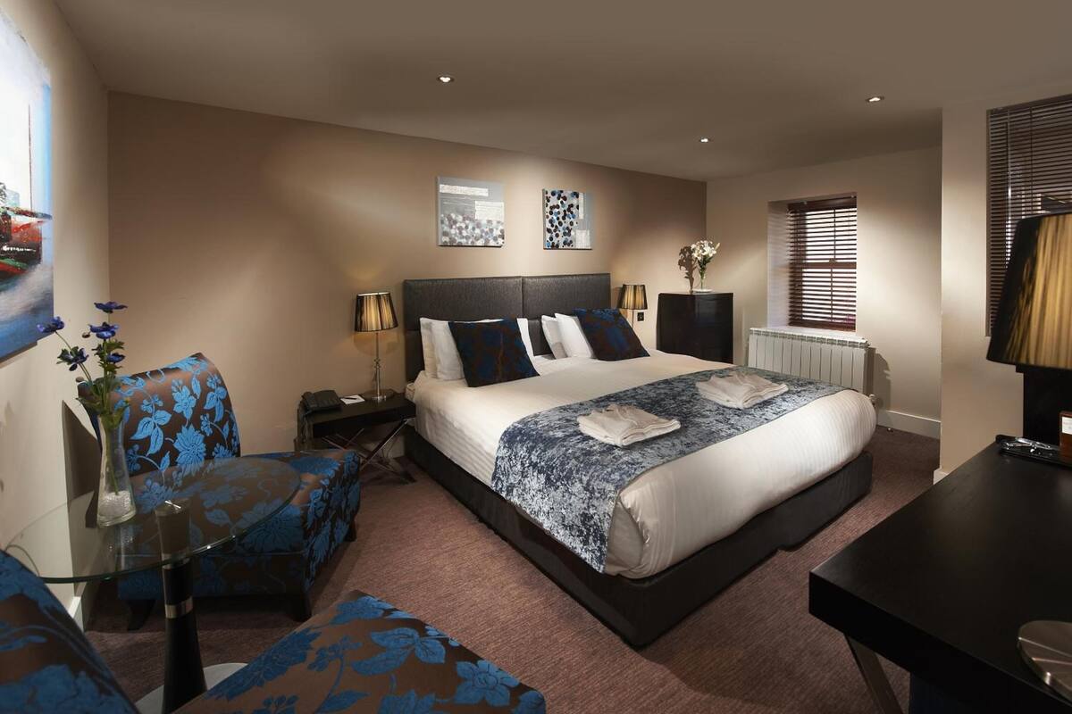 A hotel room with a large bed, a round glass table, a sofa, and a desk.
