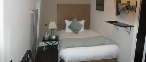 A small, neatly arranged hotel room with a single bed, bedside table, and a TV mounted on the wall.