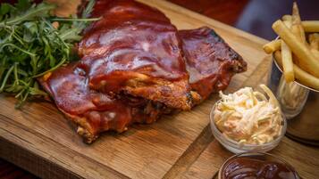 Una tabla de madera con costillas a la parrilla, papas fritas, ensalada de col y un pequeño recipiente de kétchup.