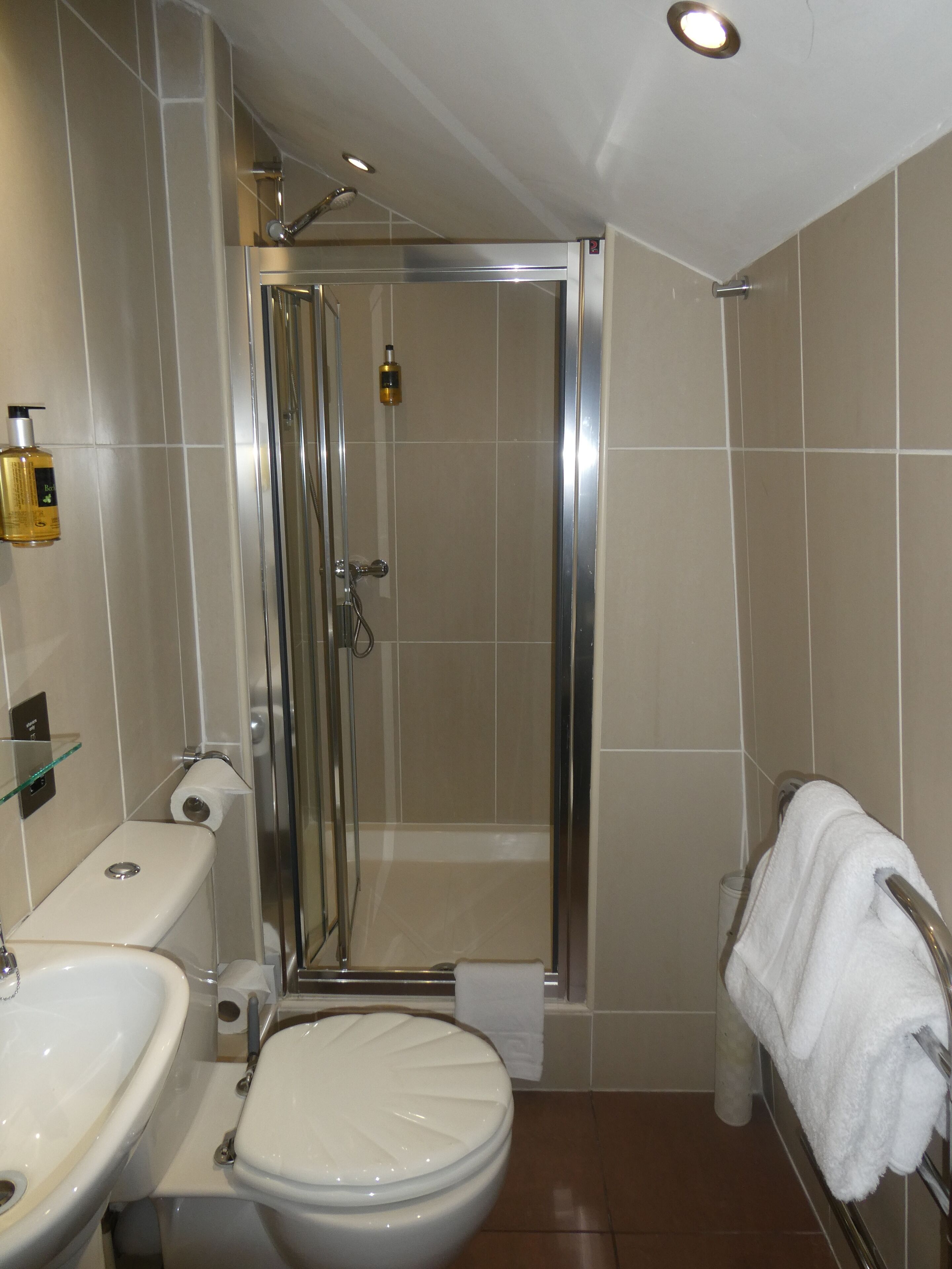 A bathroom with a shower, toilet, sink, and towel rack.