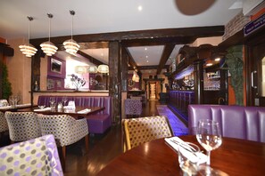 Un restaurante con vigas de madera, cabinas moradas y lámparas colgantes.