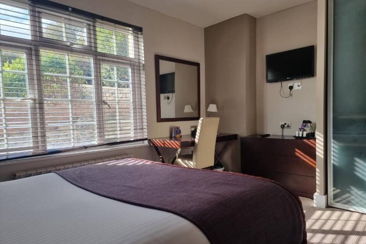 A hotel room with a bed, a desk, a chair, a television, and a window with blinds.