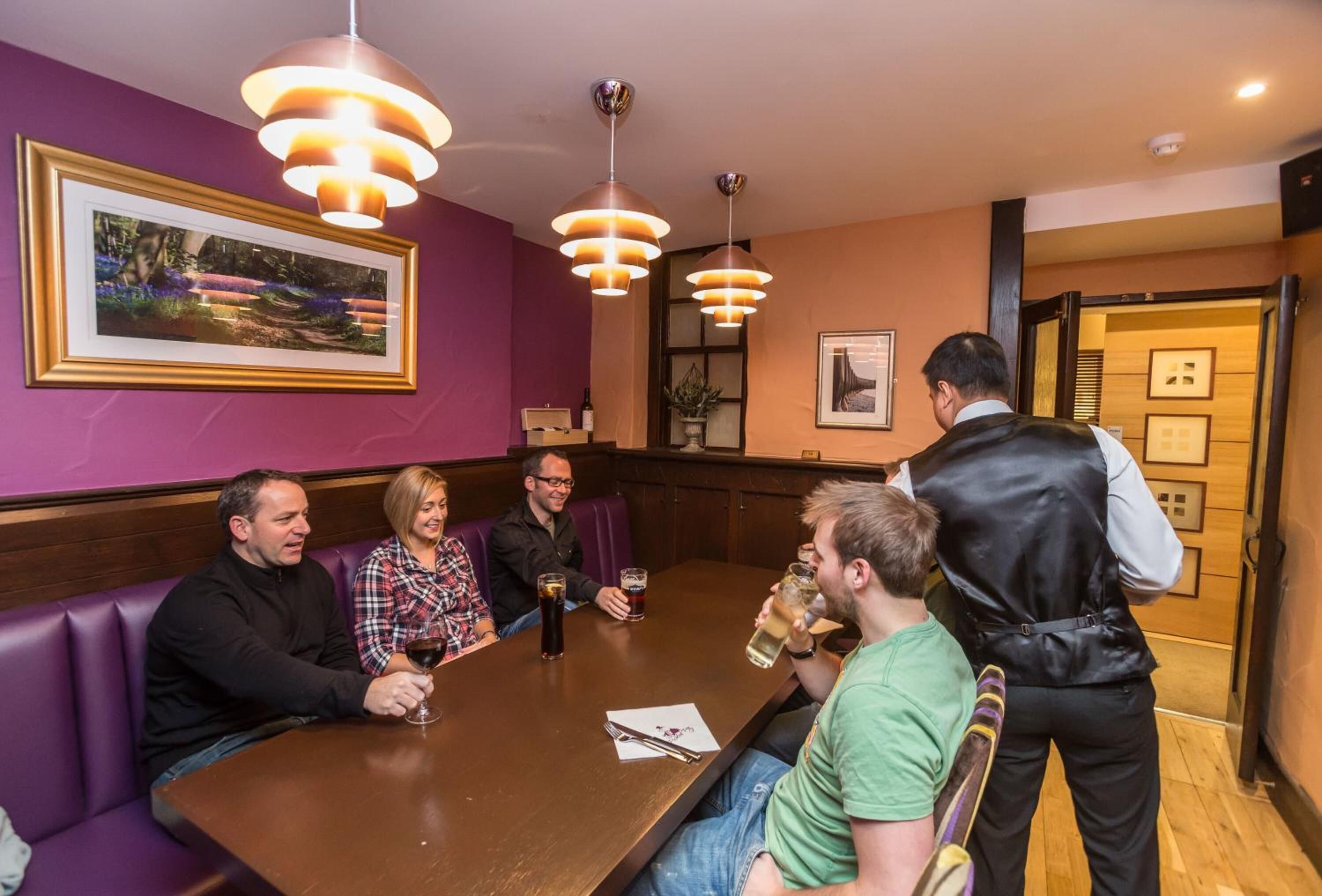 A group of people seated around a table in a restaurant with purple walls and framed pictures.