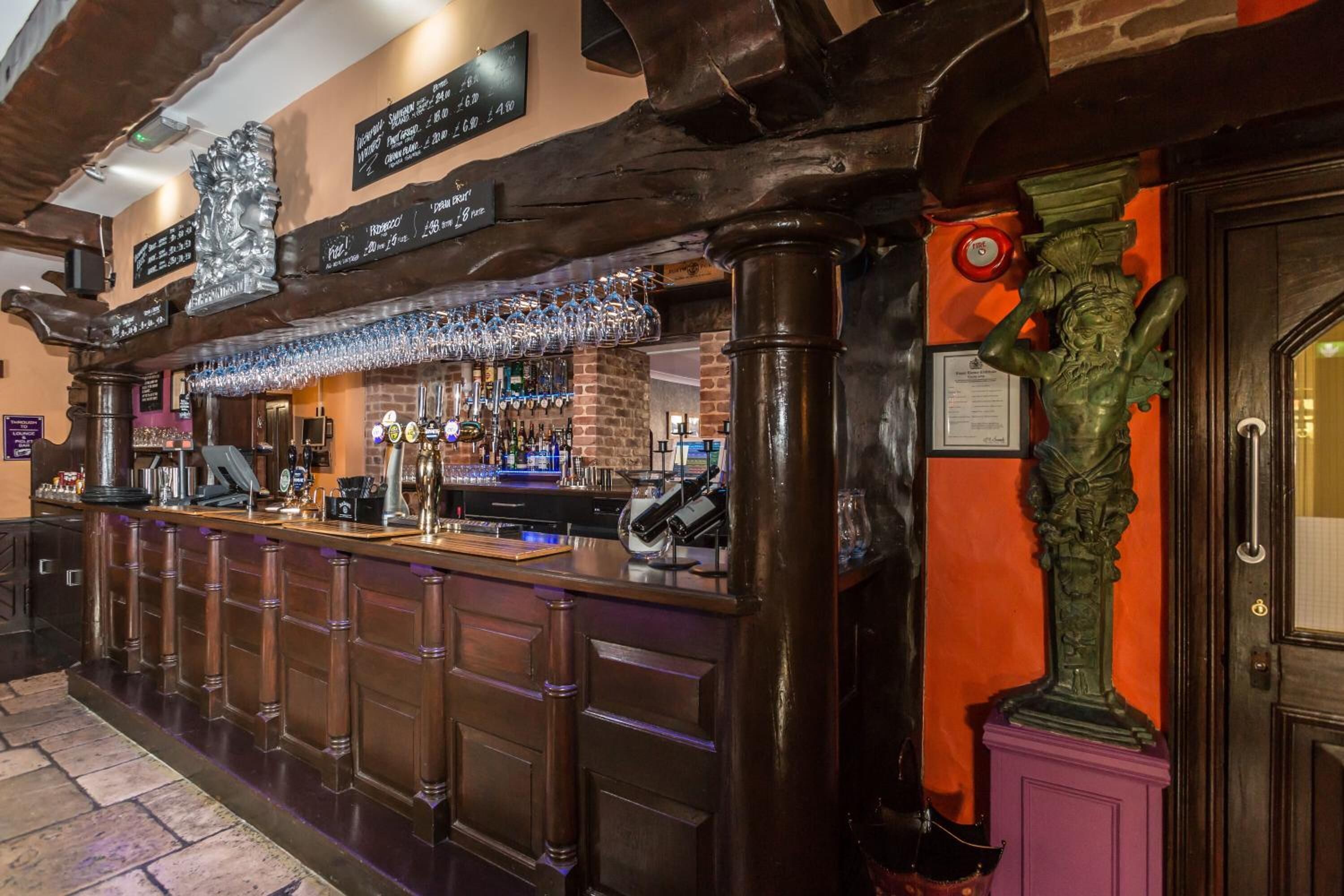 A bar area with a wooden counter, bar stools, and a variety of bottles and glasses.