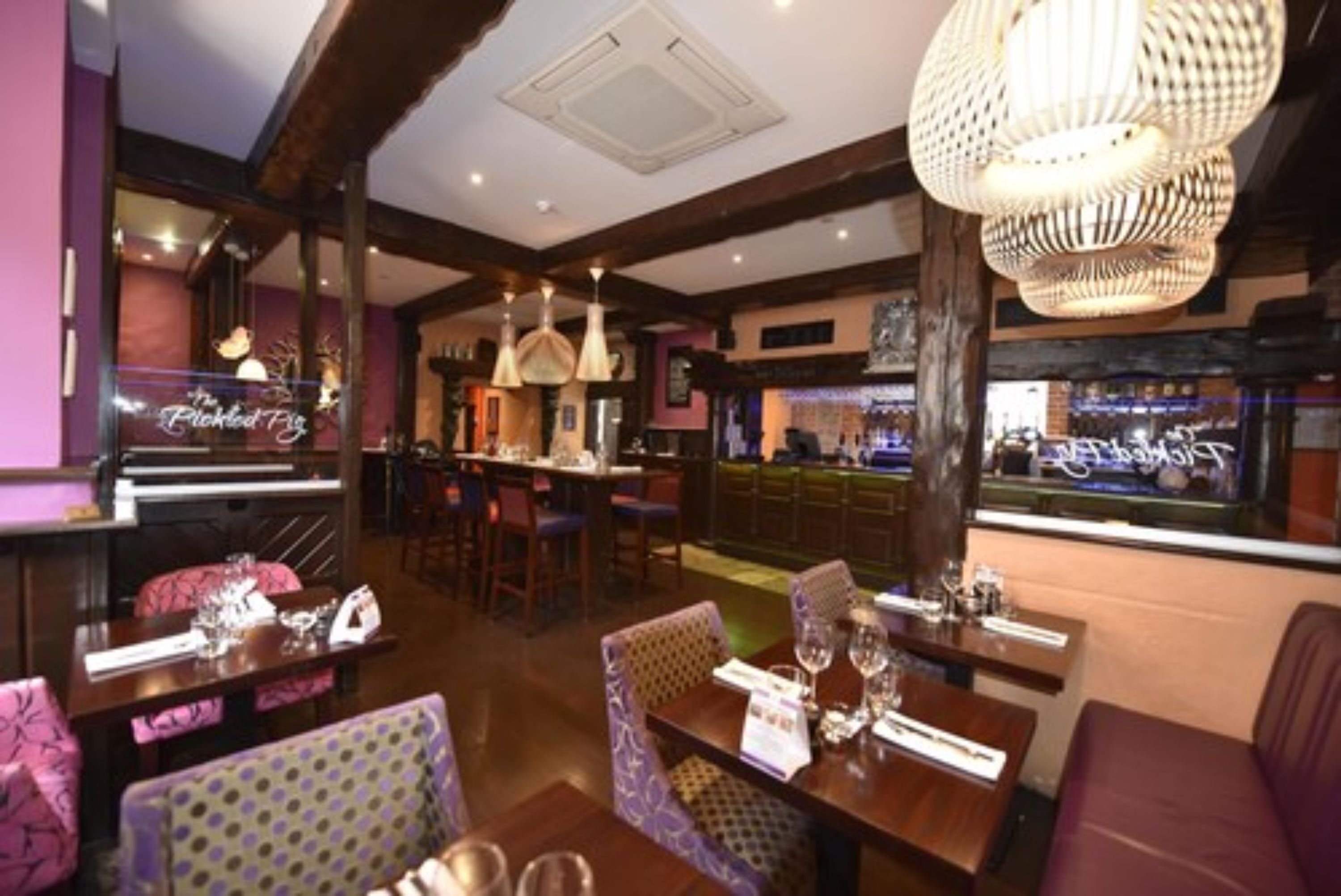 Un restaurante con vigas de madera, lámparas colgantes y asientos de bar.