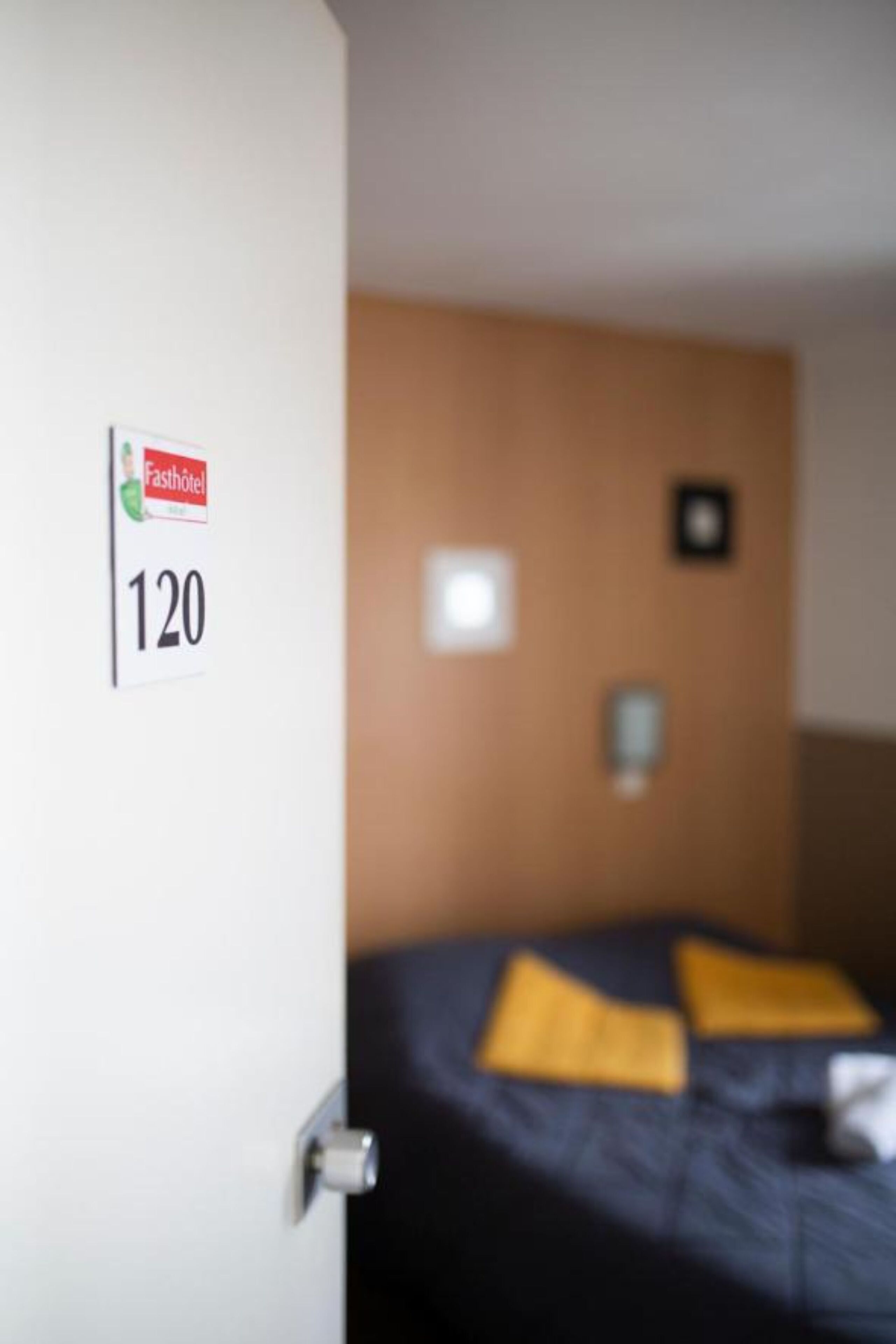 A hotel room with a bed, a sign indicating room number 120, and a wall-mounted light fixture.