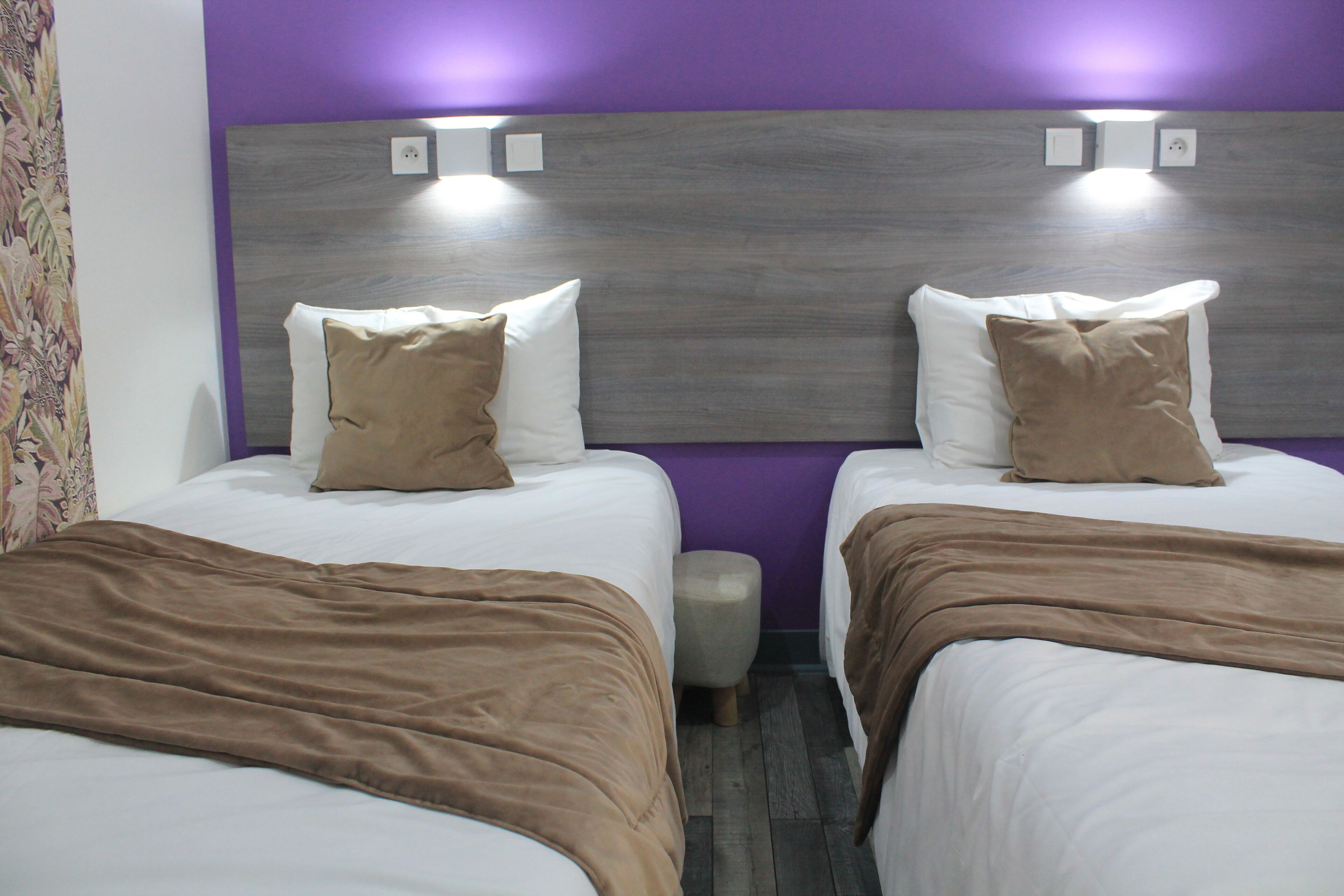 Dos camas con ropa de cama marrón, un cabecero de madera y una pared morada.