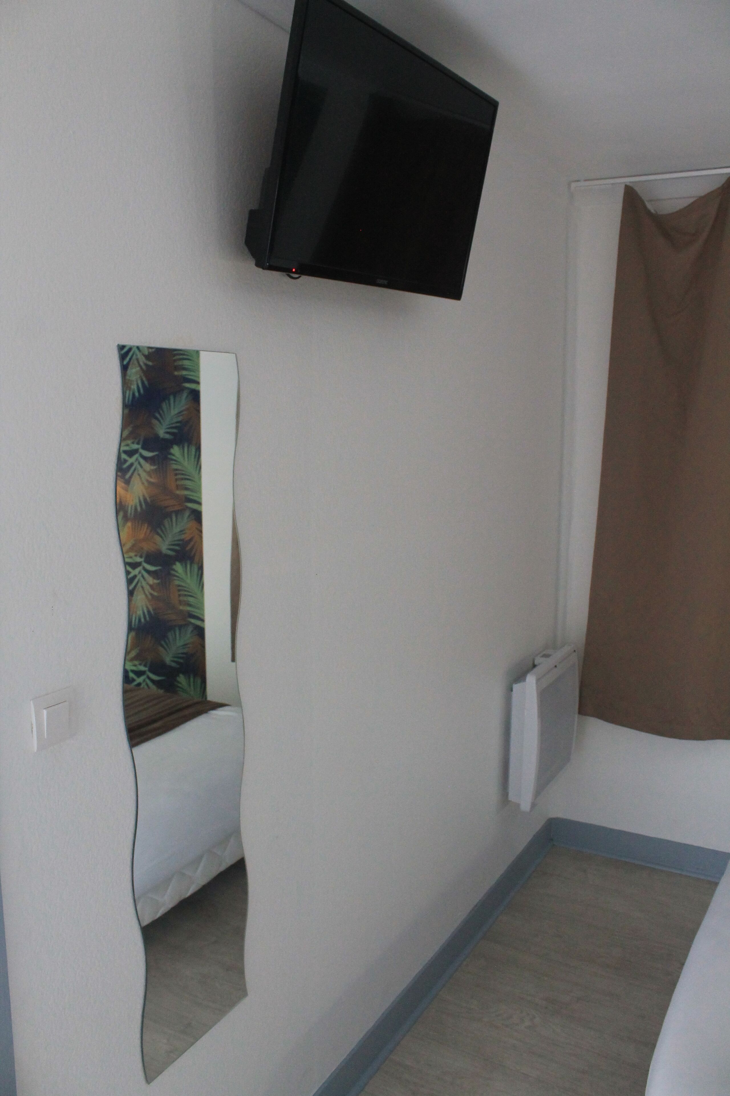 A room with a flat-screen TV mounted on the wall, a shower curtain, and a partial view of a bathroom mirror.