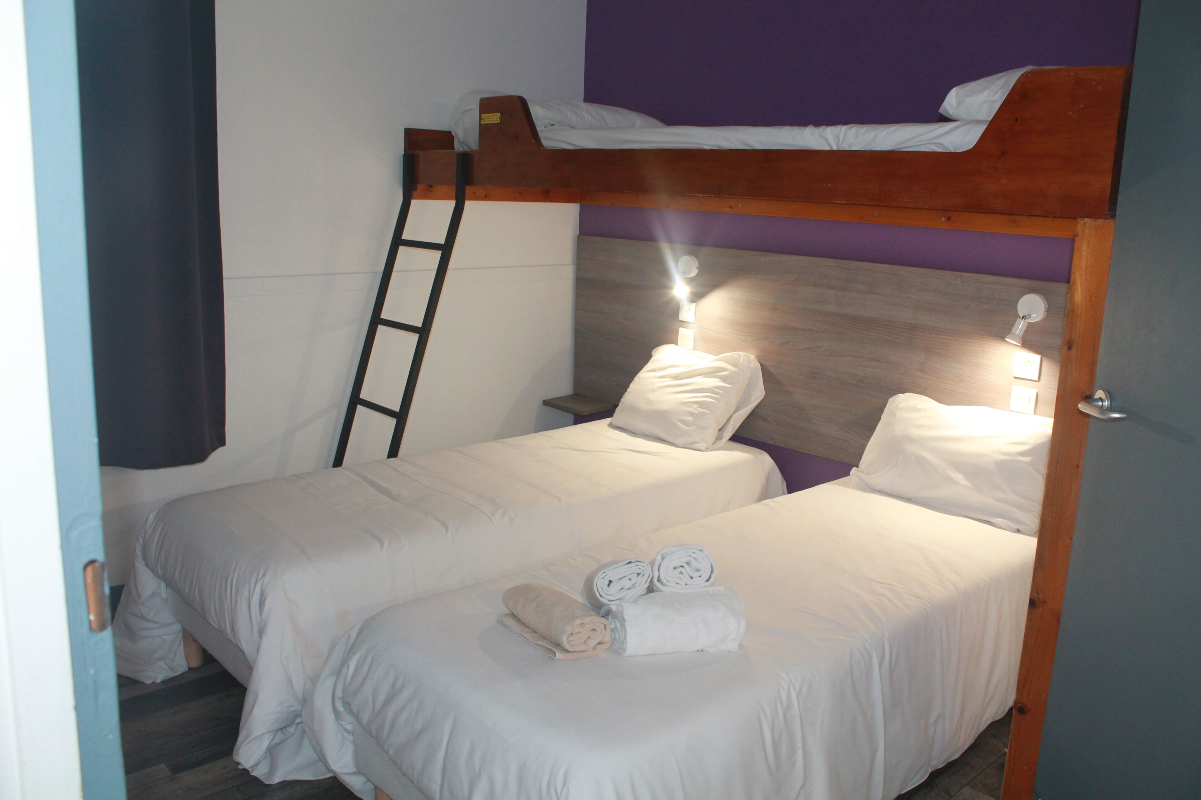 A bunk bed room with two beds, a ladder, and a bedside table with a lamp.