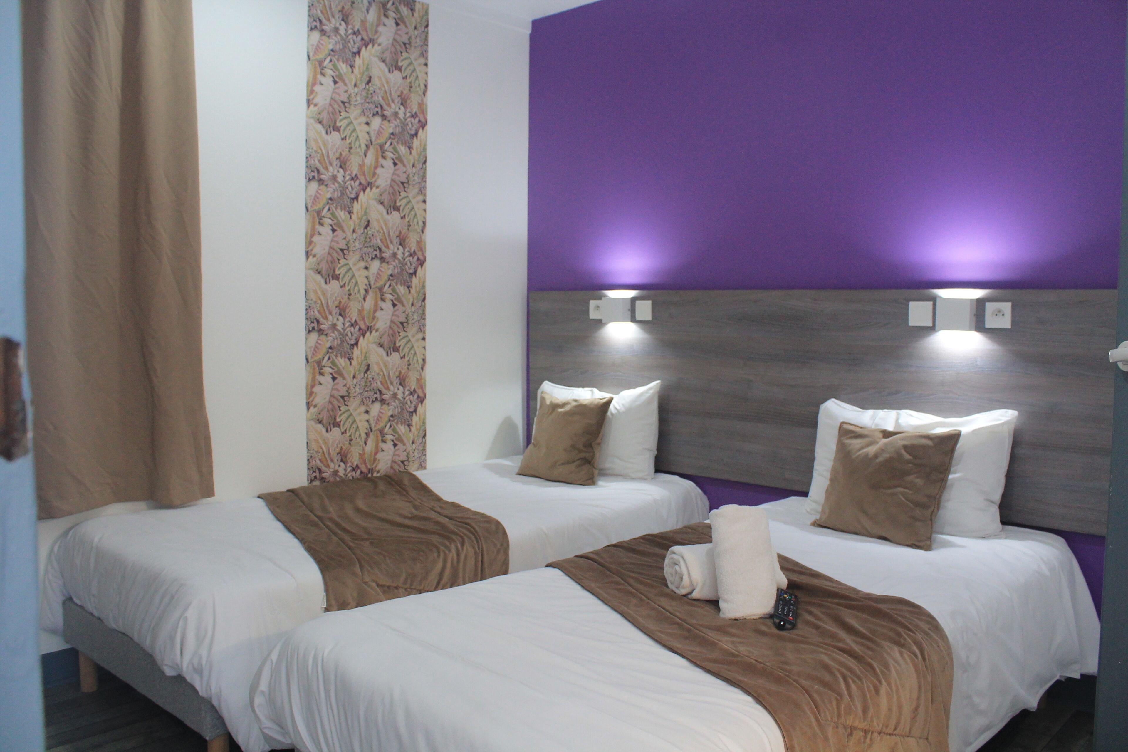 Hotellihuoneessa on kaksi sänkyä, joissa on valkoiset lakanat ja ruskeat torkkupeitot. Huoneen seinät ovat violetit ja siinä on kukkakuviollinen verho.