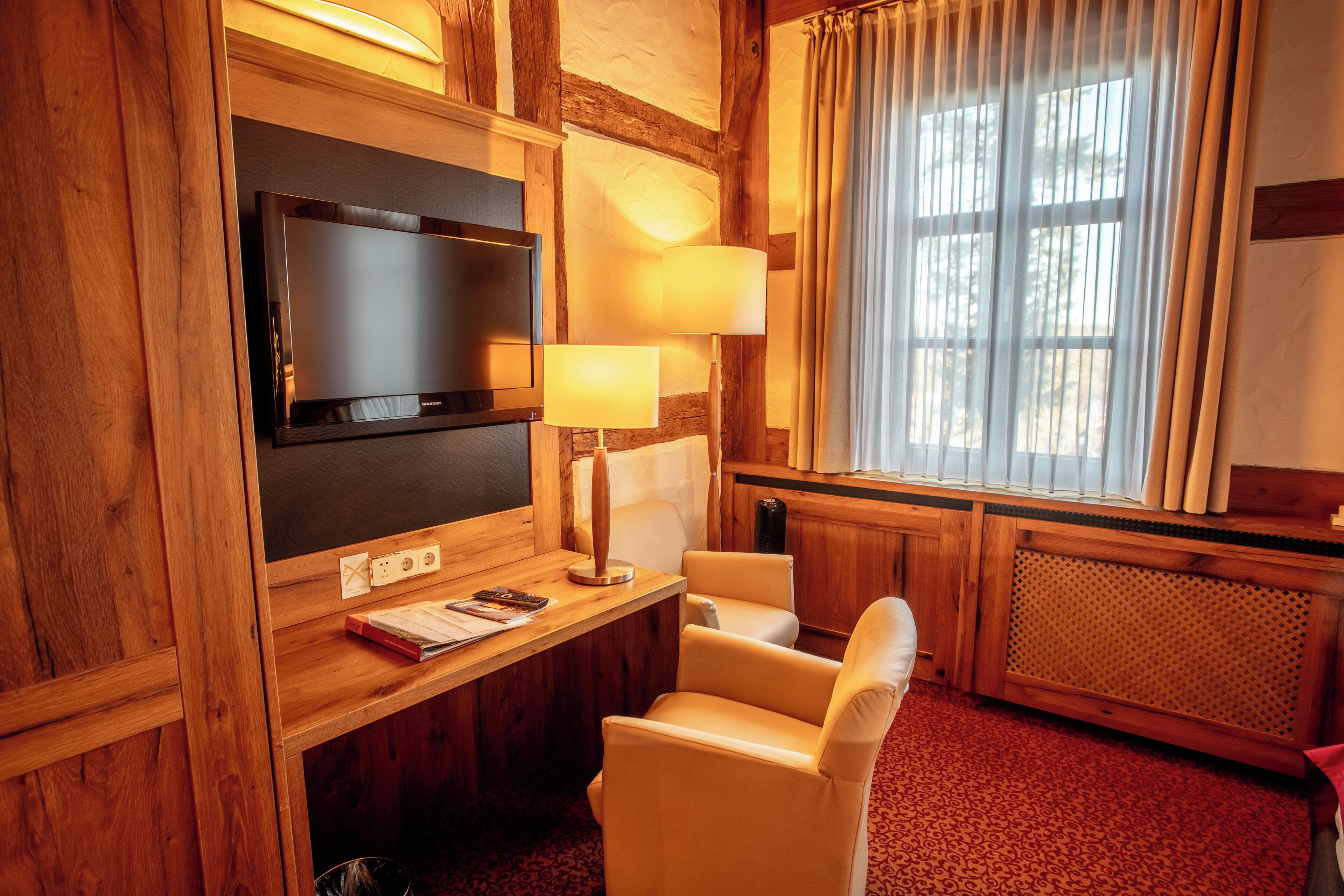 A wooden-paneled room with a television, two lamps, a desk with a book, and a chair.