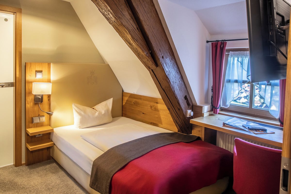 A bedroom with a bed, a desk, a lamp, and a window with curtains.