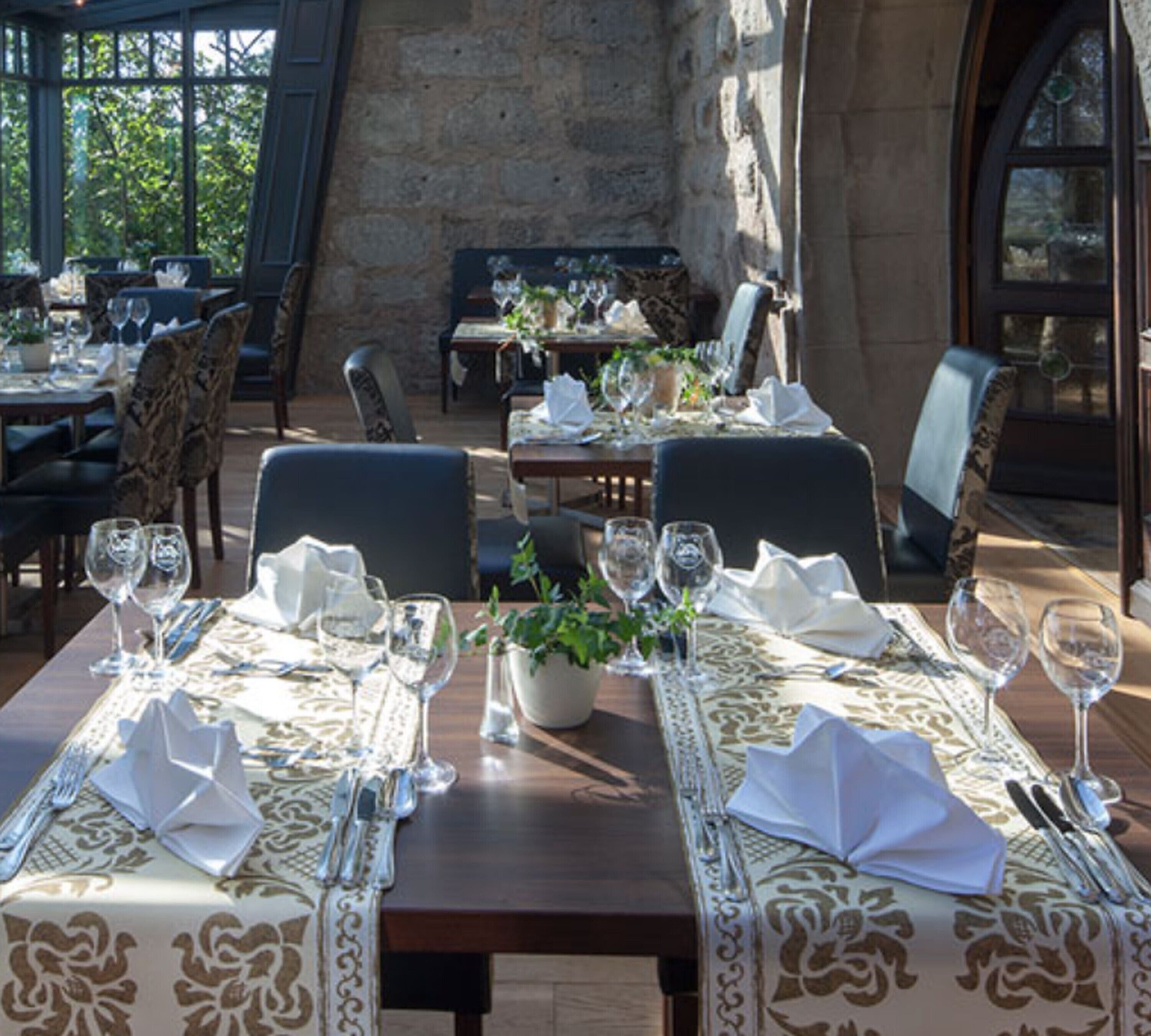 A restaurant with tables set for dining, featuring a stone wall and large windows.