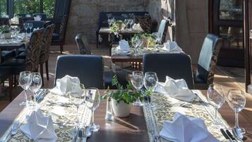 A restaurant with tables set for dining, featuring a stone wall and large windows.