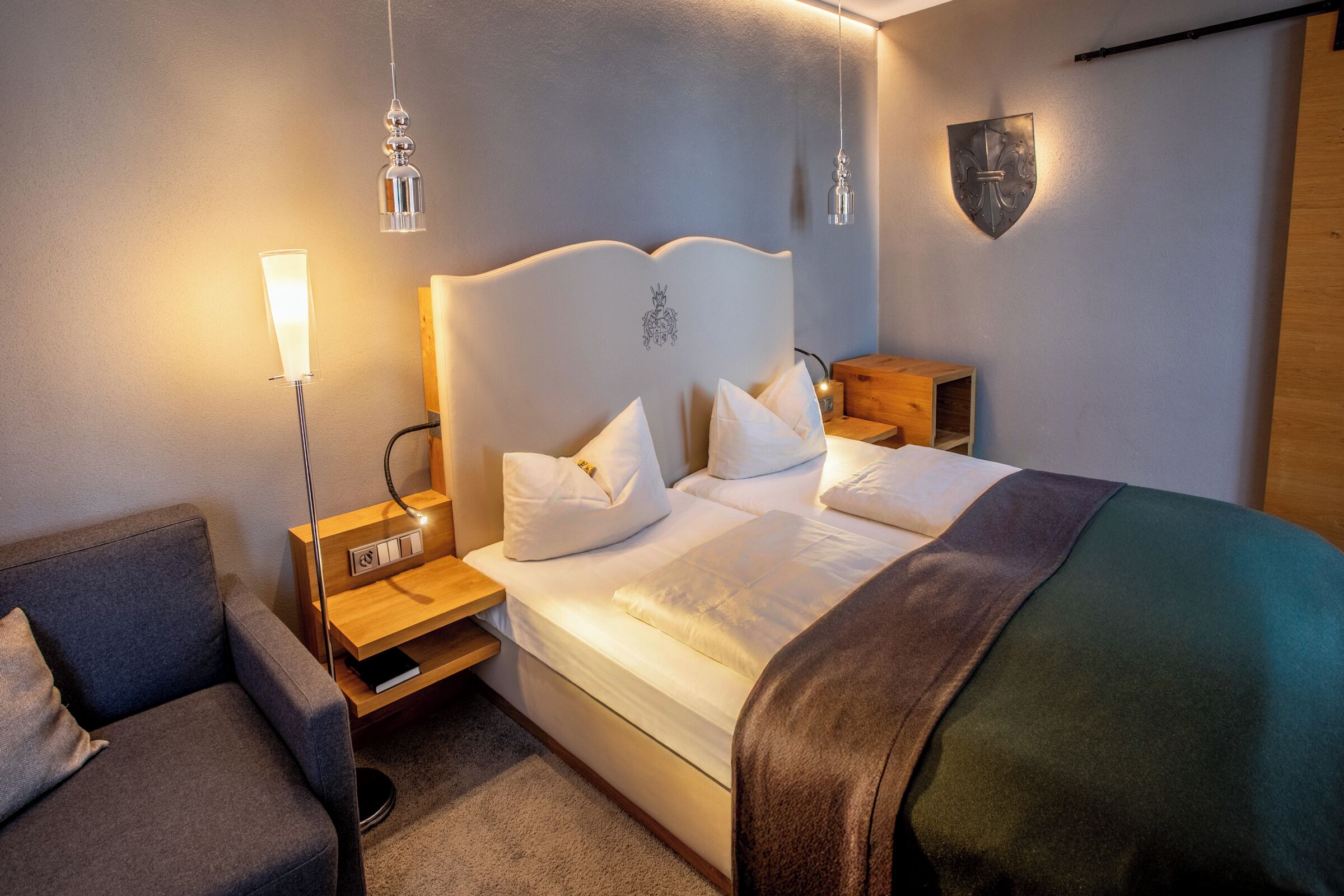 A neatly arranged hotel room with a bed, bedside tables, a lamp, and a sofa.