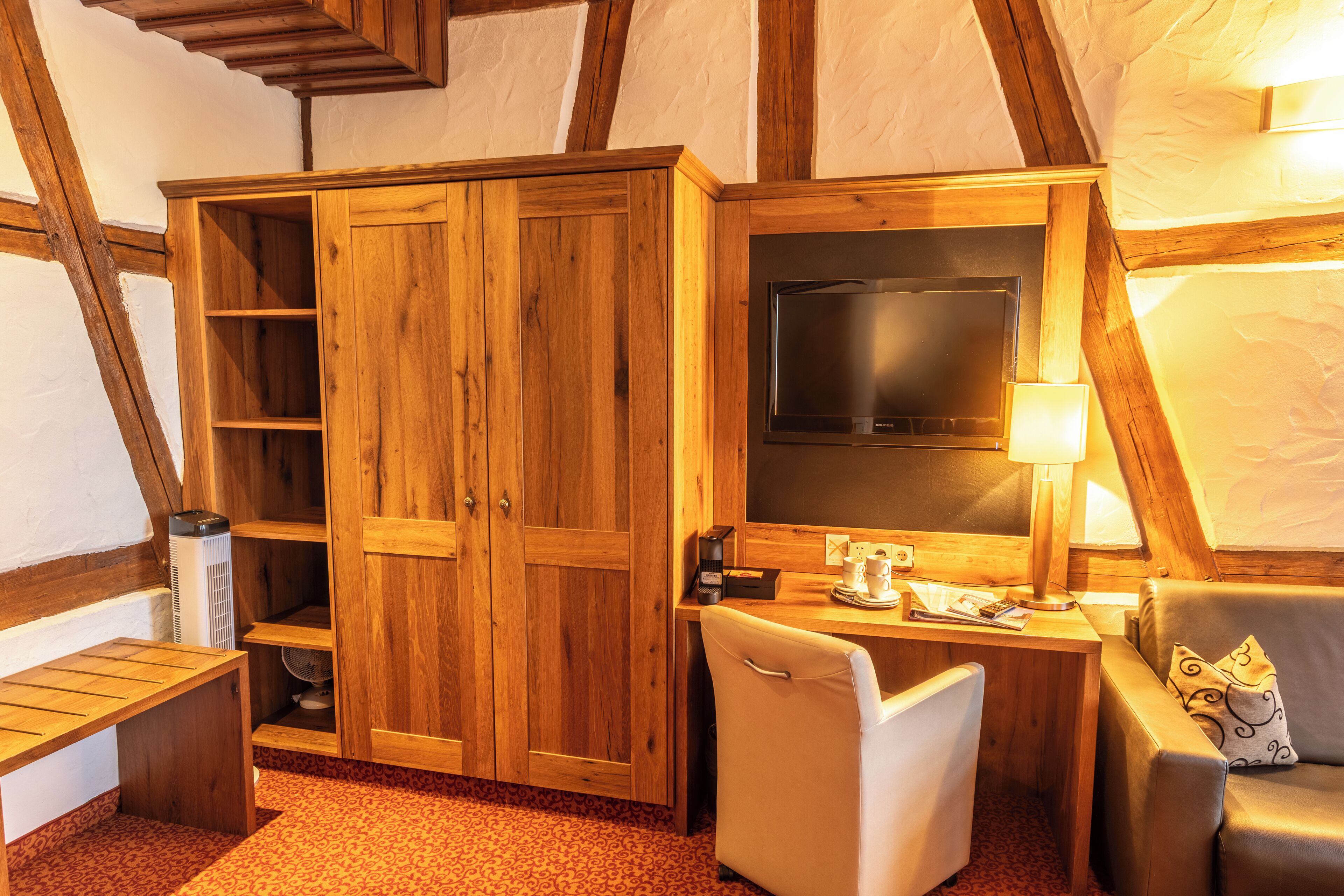 A cozy room with wooden furniture, a flat-screen TV, a desk with a lamp, and a comfortable seating area.