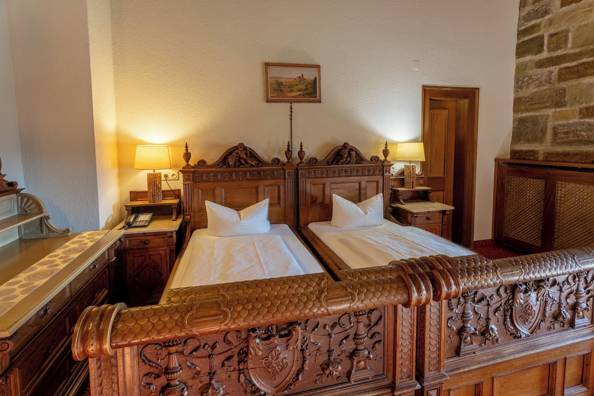 A hotel room with two wooden beds, a stone wall, and a painting on the wall.