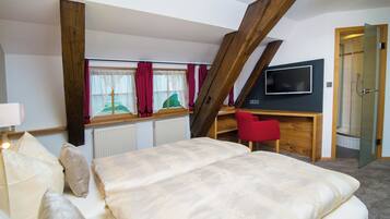 Un dormitorio con cama, escritorio, silla, televisión y ventana con cortinas.