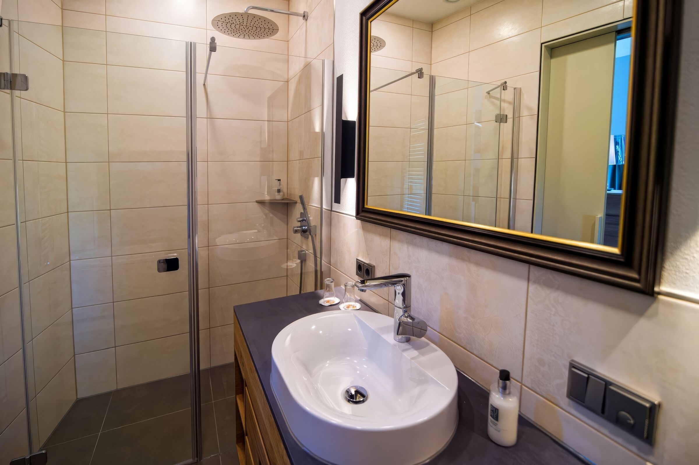 A modern bathroom with a glass-enclosed shower, a white sink, and a large mirror.