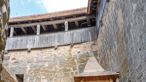 Una estructura de juego de madera con un tobogán y zona de escalada, frente a un edificio de piedra con techo de tejas.
