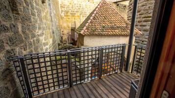 A wooden deck with a metal railing, a stone wall, and a tiled-roofed building in the background.