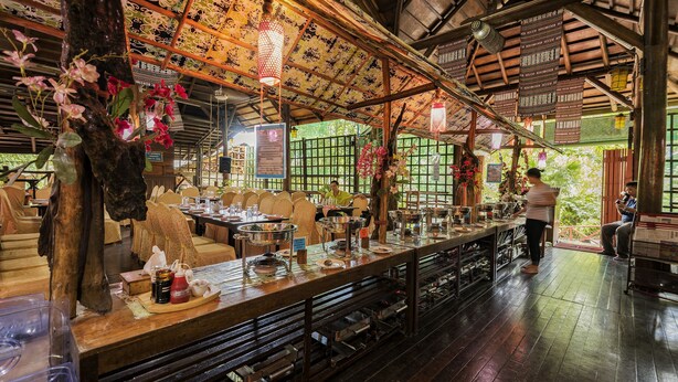 A restaurant with a long counter, wooden tables, and hanging lanterns.