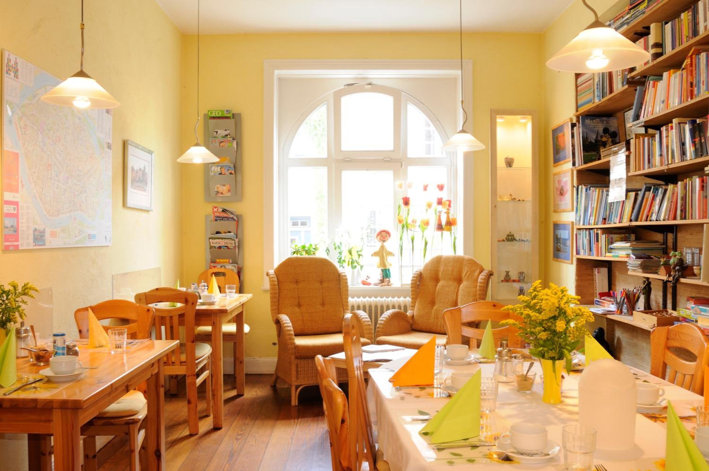 A cozy dining area with wooden furniture, a large window with a view, and a bookshelf filled with books.