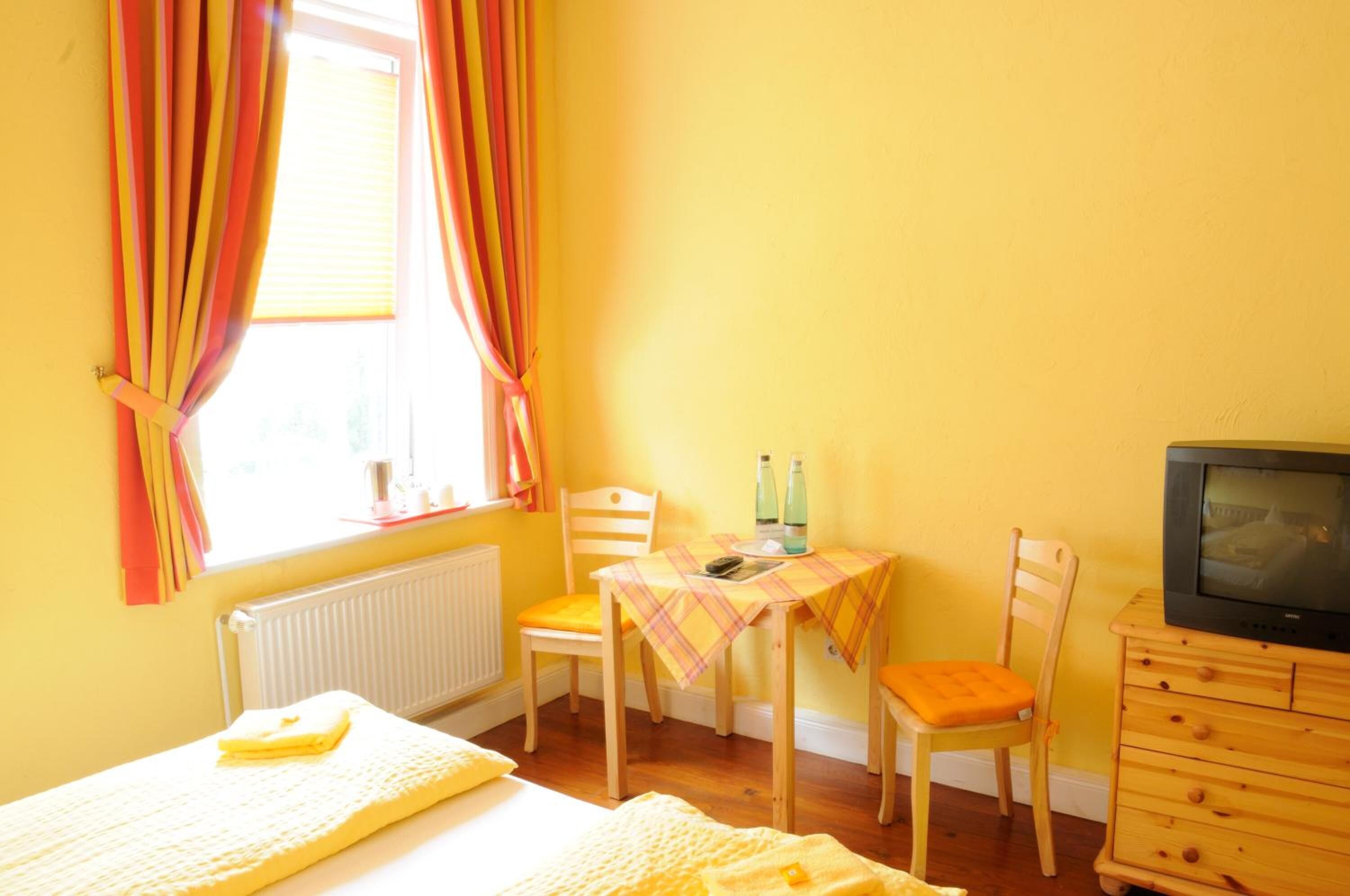 A room with a bed, a table with chairs, a television, and a window with curtains.
