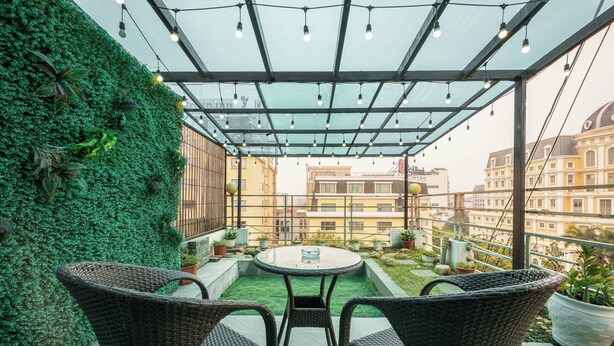A covered patio with wicker chairs, a glass table, and a green wall. - A25 Hotel - 45 Phan Chu Trinh (Hanoi)