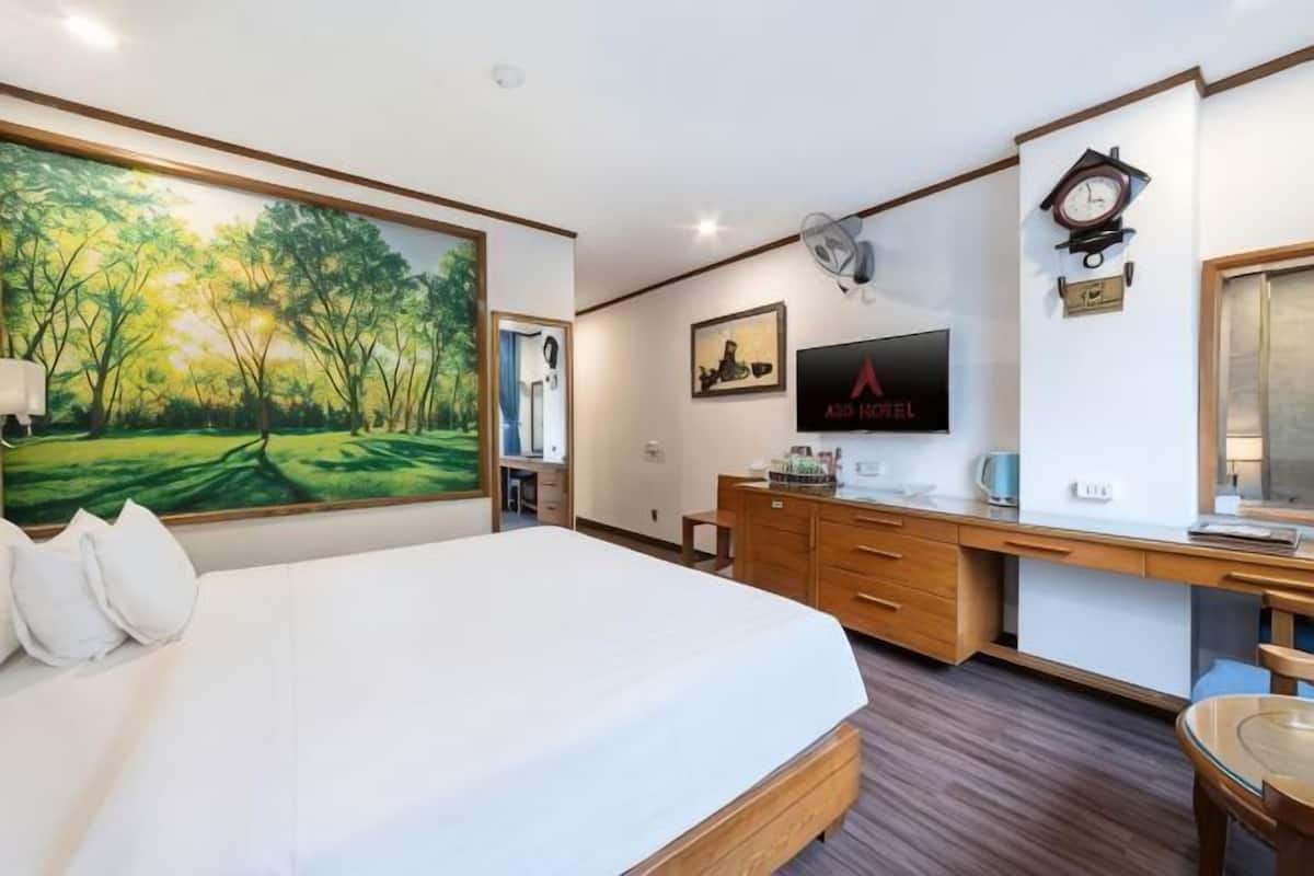 Une chambre d’hôtel avec un grand lit, un bureau avec un ordinateur, une télévision et une horloge au mur.