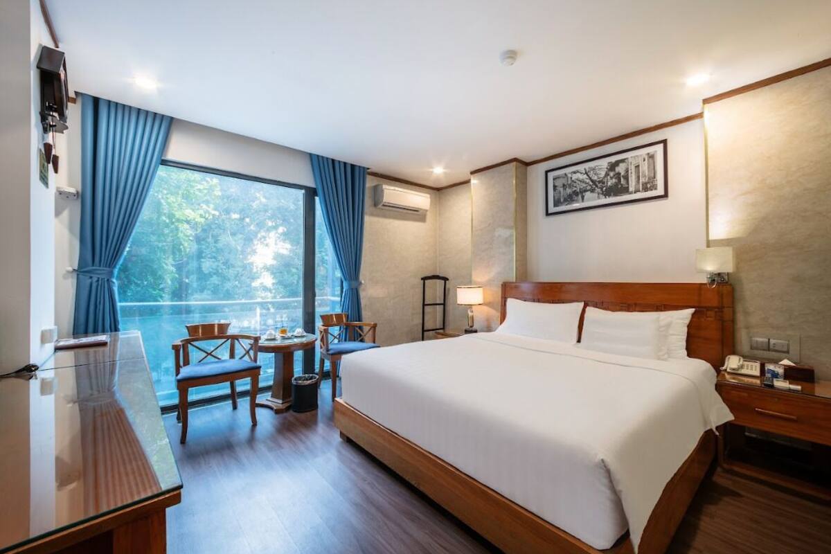 Une chambre d’hôtel avec un grand lit, un bureau, deux chaises et une vue sur les arbres par la fenêtre.