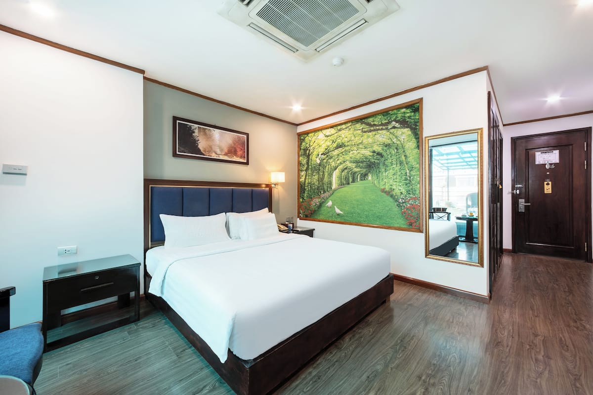 Une chambre d’hôtel moderne dotée d’un grand lit, d’une table de chevet, d’un bureau et d’une grande fenêtre donnant sur un parc.