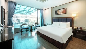 A hotel room with a large bed, a desk, a chair, a small table, and a window with curtains. - A25 Hotel - 45 Phan Chu Trinh (Hanoi)
